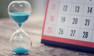 a sand timer next to a page of a calendar sitting on a table brian jackson adobe stock 408250547 1