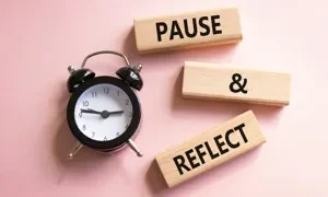 the words pause reflect printed on blocks next to a alarm clock against a pink background natallia adobe stock 1776723426