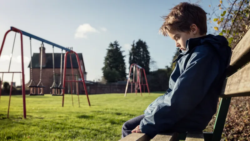 a child looking lonely while sitting on a park bench brian jackson adobe stock 100207516