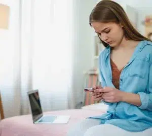 a teenage girl looking anxiously at her phone in her bedroom halfpoint adobe stock 357858561