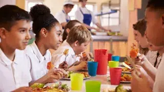 children have school lunch together with lunchtime supervisors in the background monkey business adobe stock 112287238